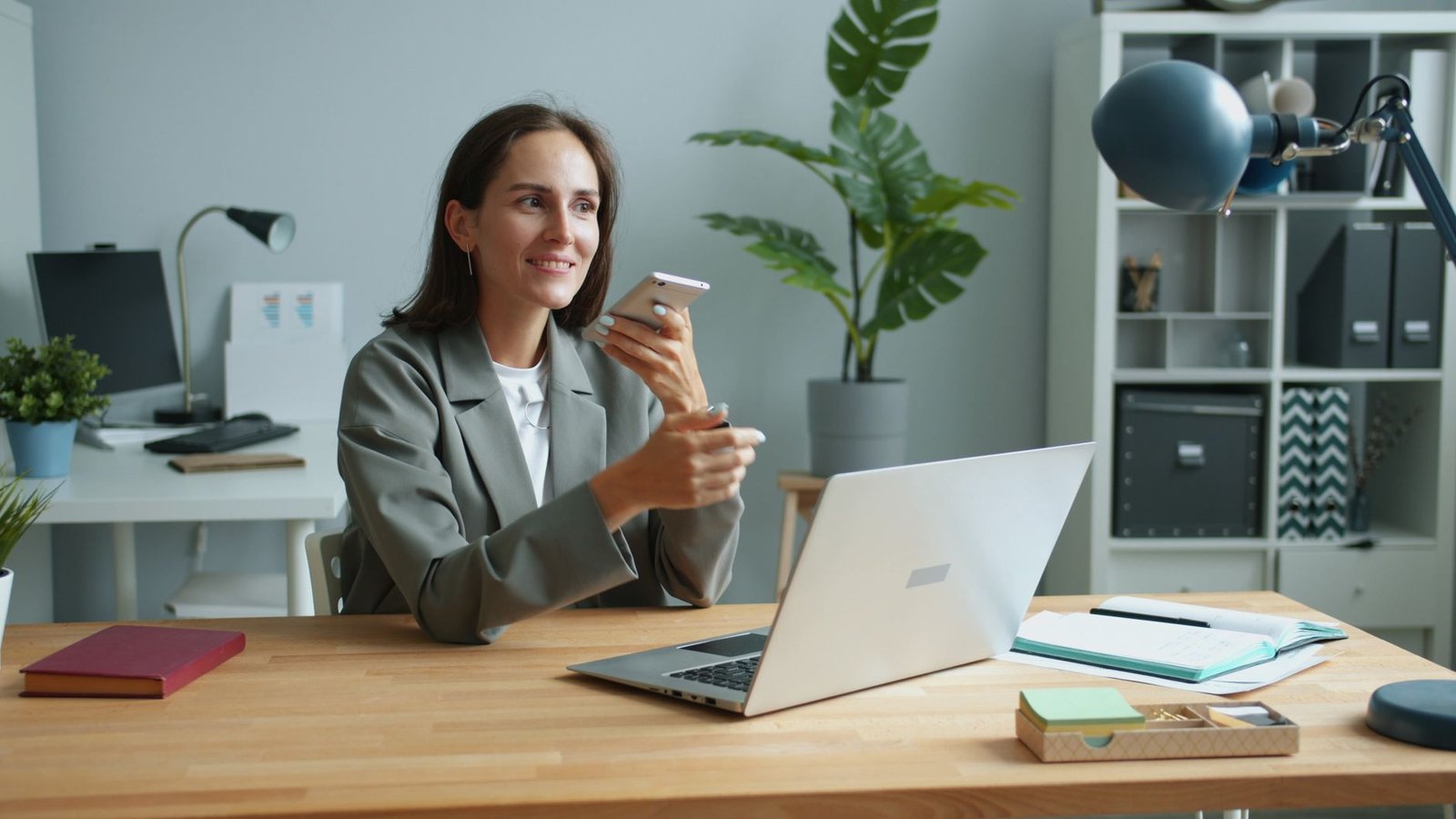 confident businesswoman using smartphone and laptop in modern office researching keynote speakers for an upcoming event