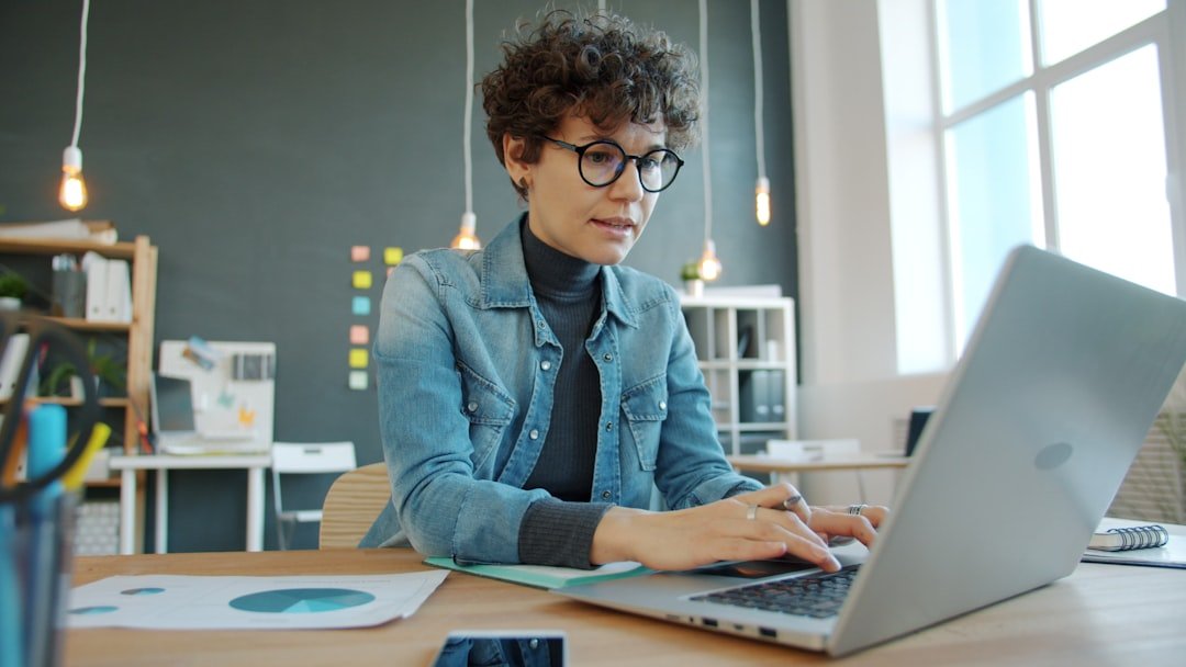 serious woman typing and writing speaker website headline on laptop in creative office