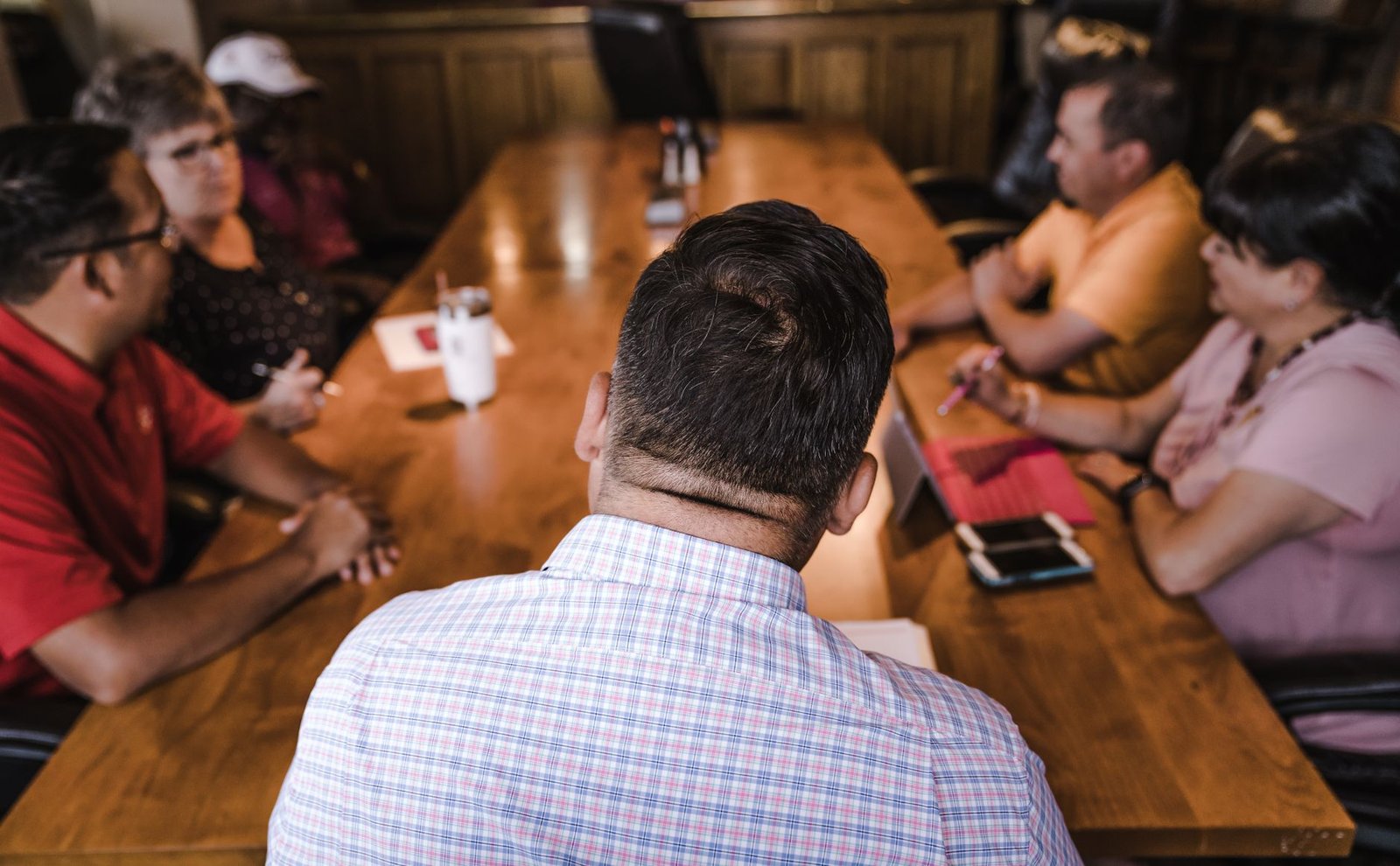 event planning committee discussing a speaker booking decision around a table representing the people a speaker never meets