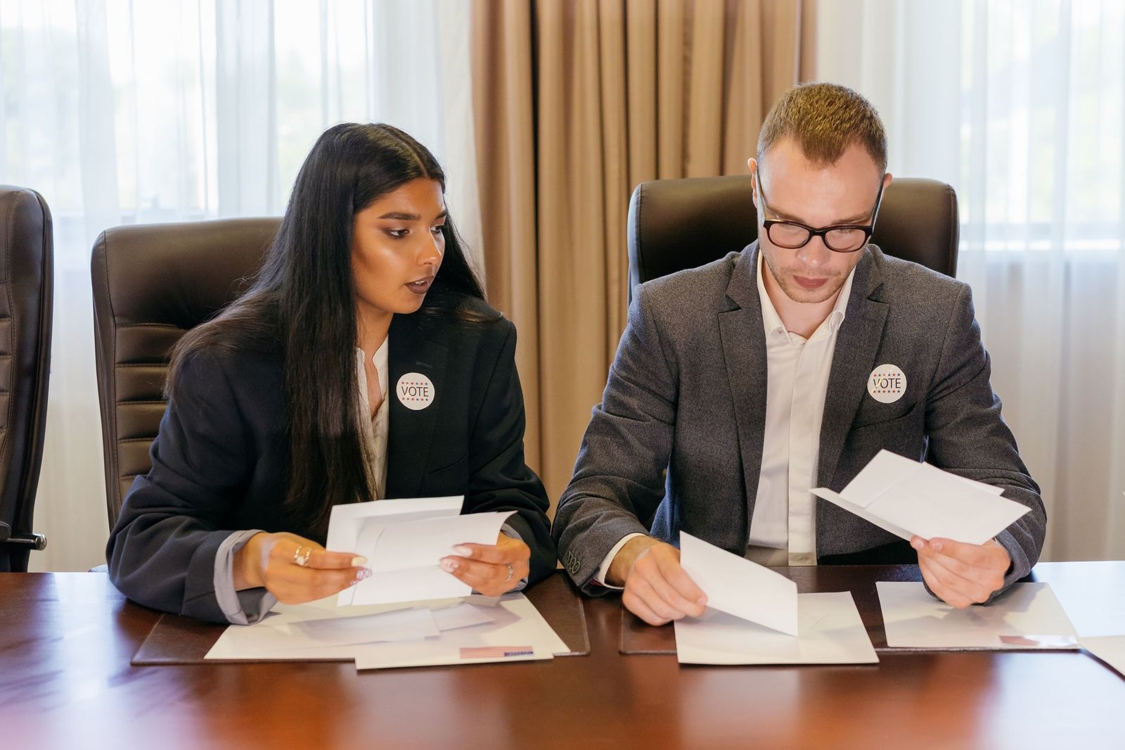 two professionals reviewing documents at conference table representing event organizer deciding between two similar keynote speakers