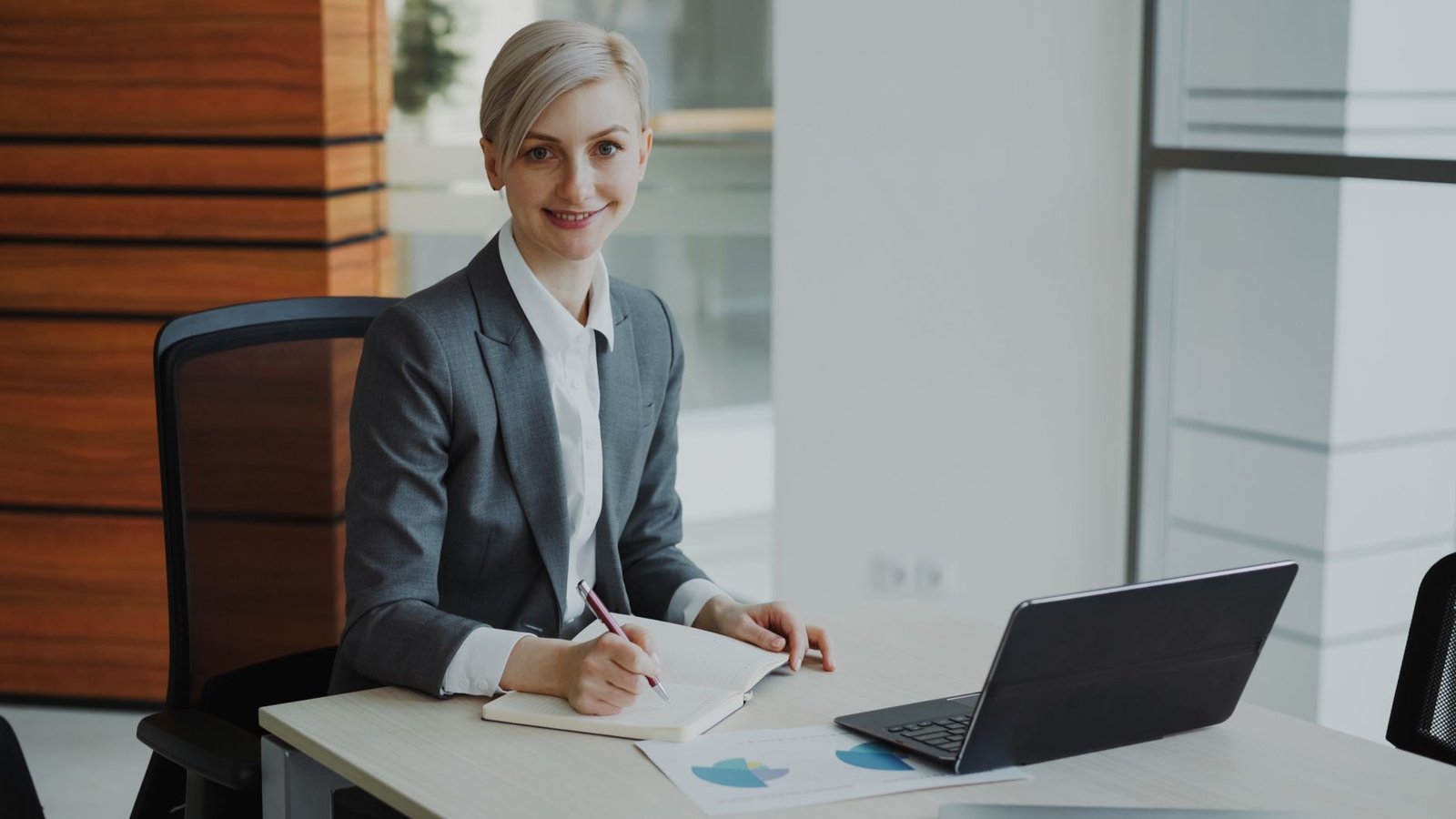 confident businesswoman taking notes in modern office representing a speaker preparing the foundations needed before pitching for their first paid keynote gig