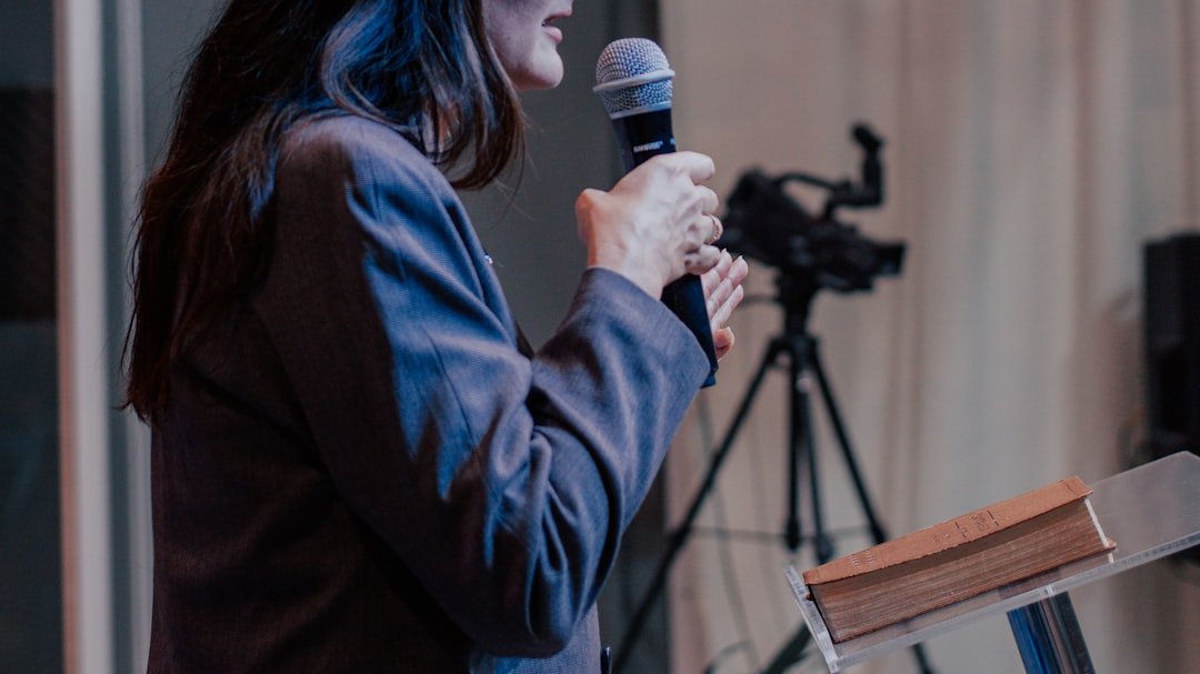 woman standing at conference podium holding microphone being introduced on stage representing the outcome of a well written keynote speaker bio