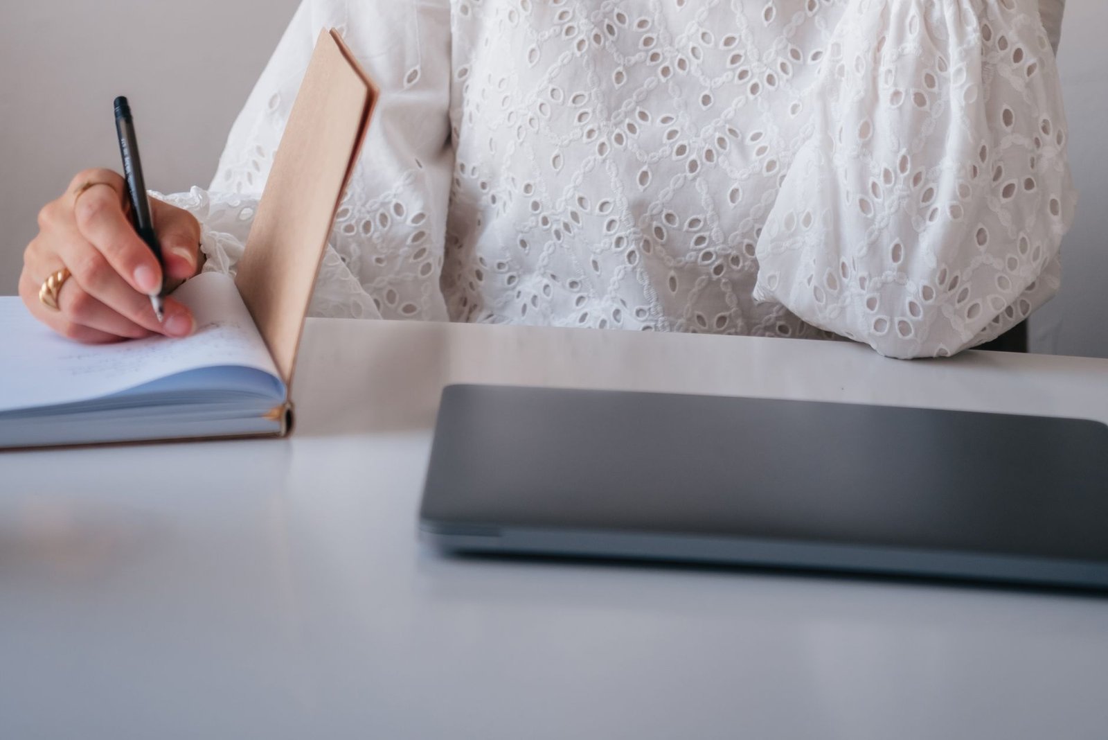 professional woman writing speaker bio in notebook while working on laptop at desk