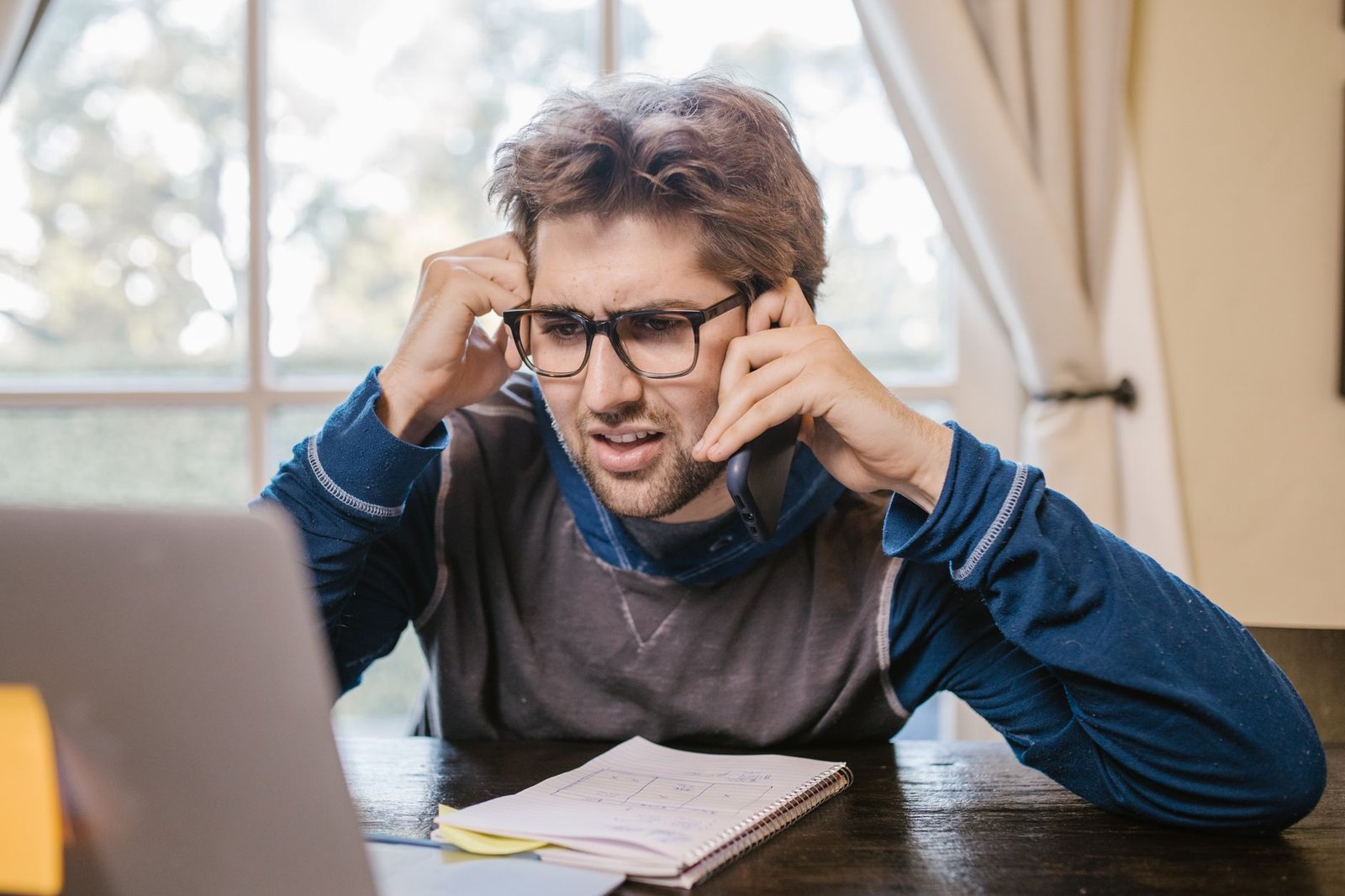 confused professional looking at laptop and phone representing a speaker puzzled by website traffic that never turns into booking inquiries