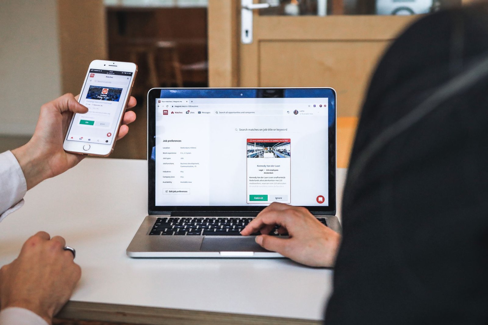 professional using smartphone and laptop together representing a speaker comparing their LinkedIn profile against their own website for bookings